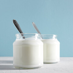 Yogurt, kefir or fermented milk product in glass jars on a white table. White and blue background. Healthy food concept