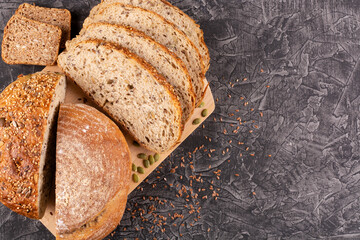 Slices and halves of whole wheat flour bread with flax seeds, sesame seeds, pumpkin seeds, sunflower seeds on a wooden board on a black background. Bread without yeast, with sourdough. Space for text.