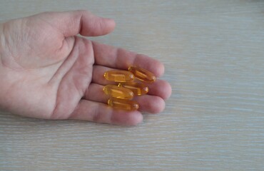 In a woman's hand are vitamins in yellow capsules.	