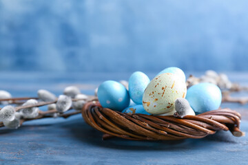 Nest with painted Easter eggs and pussy willow branches on blue background
