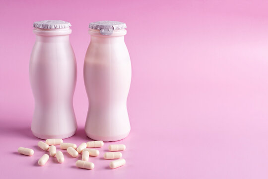 Two bottles of milk yogurt (kefir) and capsules with probiotic on a pink background. The concept of an alternative to pills and a healthy diet. Space for text.