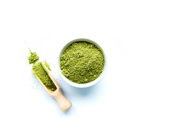 Superfood green powder in a small white bowl with scoop on white background. Matcha tea powder, spinach, chlorella, moringa, wheatgrass, or broccoli powder. Top view, free space for text or design.