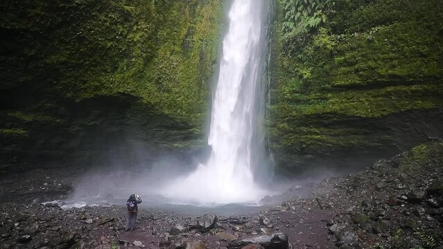 woman standing in front of strong waterfall filming with phone