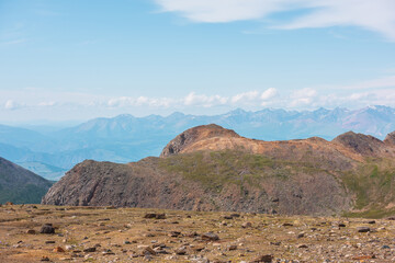 Dramatic alpine landscape with large mountain top in sunlight against high mountain range with snow under clouds in blue sky. Colorful mountain scenery with sunlit sharp rocks at changeable weather.