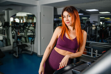 Fototapeta na wymiar Portrait of sportive fit woman in gym interior, beautiful healthy female posing at modern sports hall with equipment