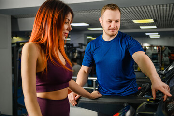 Fototapeta na wymiar Trainer adjust, press buttons at treadmill jogging track for pretty woman, gym customer, sportive lifestyle