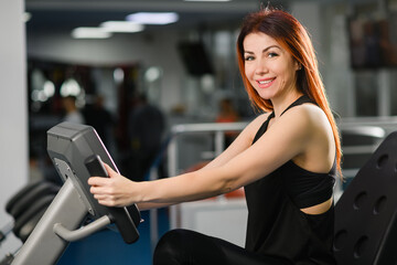 Portrait of smiling fit woman sit at gym machine for sport fitness cardio exercise, healthy active lifestyle