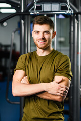 Fototapeta na wymiar Portrait of sportive fit man in gym interior, beautiful healthy male posing at modern sports hall with equipment
