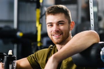 Portrait of smiling handsome young fit man with beard in gym interior with modern equipment machines, healthy active lifestyle