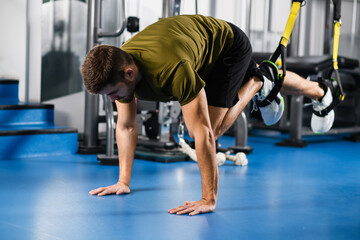 Fototapeta na wymiar Young man making workout exercise for legs with trx fitness straps at modern gym interior.