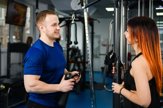 Woman customer talking with sport trainer coach at modern gym hall interior for workout exercises healthy plan