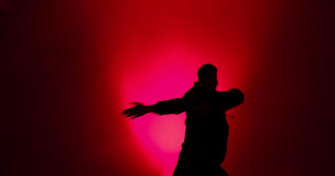 Silhouette of young man doing hiphop style dance in red light and smoke
