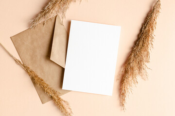 Invitation or greeting card mockup with envelope and dry plant decorations on beige background