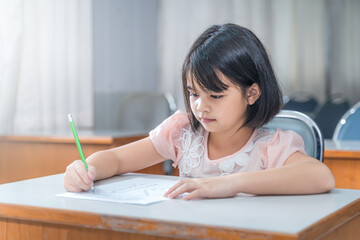 A female Asian kid student concentrate writing on the examination paper in the class