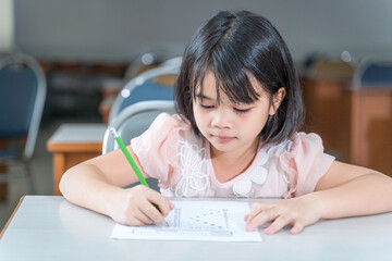 A female Asian kid student concentrate writing on the examination paper in the class