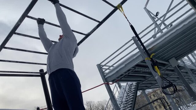 Young athletic man doing pull-ups on horizontal bar during his outdoor winter workout 