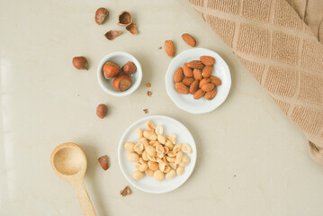 Peanut, almond, hazelnut in a white plate, brown kitchen towel, wood spoon on a kitchen top 