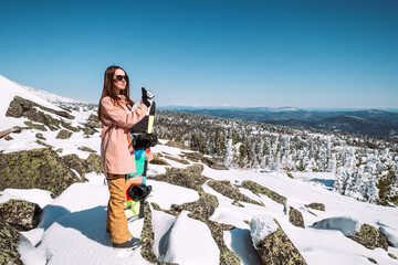 Russia. Sheregesh. Girl snowboarder in black sun goggles in winter in sunny weather outdoors among...