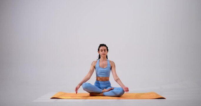 Young woman stretching arms while meditating in lotus position over white background