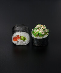 maki sushi with salmon and chuka seaweed on black background closeup