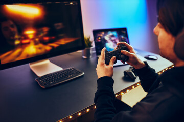 Man playing video game at home. Gamer holding gamepads sitting at front of screen. Streamer playing...