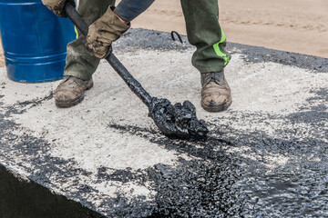 A construction worker is engaged in dirty manual work to repair and apply black bitumen...