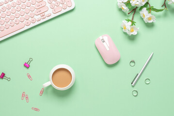 Top view office desk. Women's workspace of a blogger or freelancer. Keyboard, coffee cup and stationery on green pastel background. Spring stationery still life.