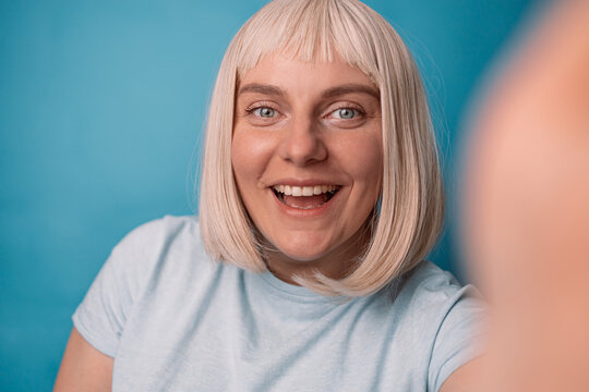 Portrait of pretty young woman looking at camera and smiling while taking selfie photo isolated on blue background, people lifestyle concepts