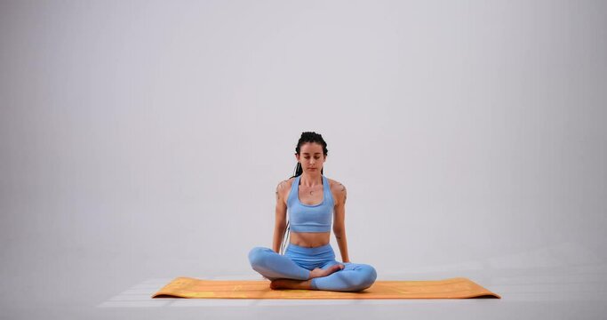 Young woman meditating in lotus position and stretching arms over white background
