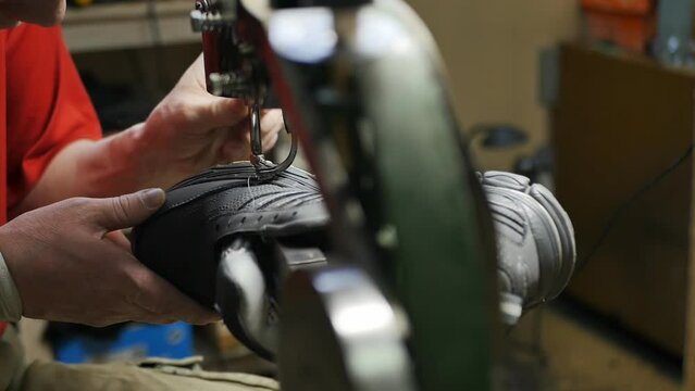 the process of repairing shoes on an old mechanical fully manual typewriter, a male shoemaker sews a seam of a sneaker with a sharp needle, rotating the drive of the machine with his hand