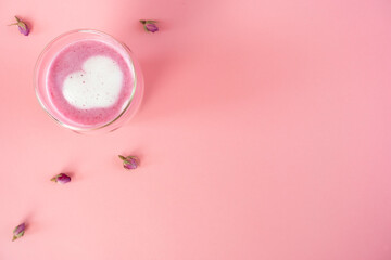 Pink rose milk with rose petals. Heart-shaped foam in a glass of moon milk. Healthy drink. Top view. Copy space.