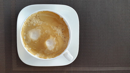 White cup with coffee on a brown background. Brewed coffee with froth