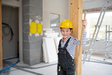 cool boy with yellow helmet posing on construction site in a house with broom