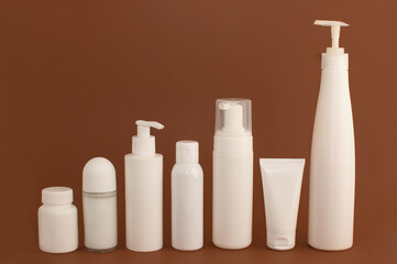 different white bottles and tubes for cosmetics on a brown background with space for text