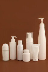 different white bottles and tubes for cosmetics on a brown background with space for text