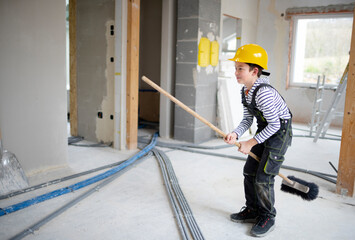 cool boy with yellow helmet posing on construction site in a house with broom