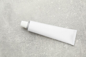 Blank white tube of ointment on light grey table, top view. Space for text