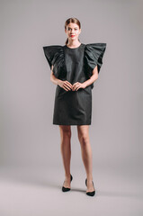 Fototapeta premium Oversize dress in black. Elegant cocktail midi dress with ruffles on massive shoulders. Beautiful young lady posing in studio. Elegant female fashion, summer evening look.