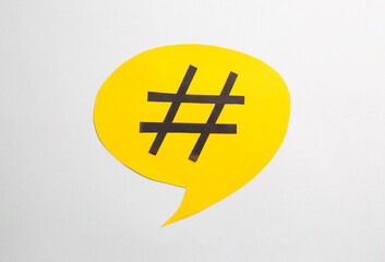 Fototapeta premium Yellow paper speech bubble with hashtag symbol on white background, top view