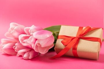 Pink tulips and a gift box on a pink background. Side view. Spring bouquet. Holiday concept. Women's Day, Valentine's Day, Easter, birthday. Copy space.