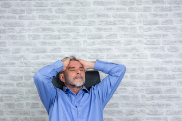 Man at home having a headache at the office with grey brick wall, copy space. health care, stress, old age and people concept - senior man suffering from headache at home office