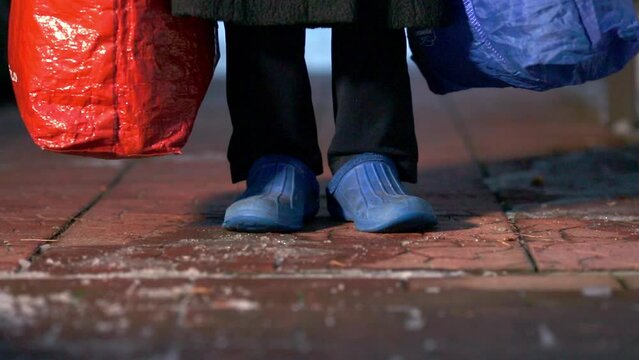 feet of refugees or homeless people in dirty cheap shoes. A faceless woman with large bags in her hands