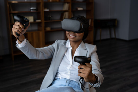 Happy joyful black woman using virtual reality software for relaxation at work, excited african american female employee wearing vr glasses holding joysticks playing video games. Selective focus