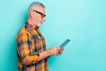 Photo of cheerful man pensioner dressed checkered shirt glasses reading device empty space isolated teal color background