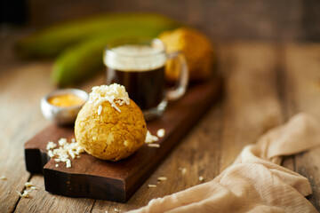 Ecuadorian bolon de verde or green plantain dumplings stuffed with cheese and accompanied by a traditional coffee. On a wooden background. - obrazy, fototapety, plakaty