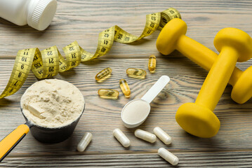 Protein, creatine, omega 3, dumbbells and measuring tape on a wooden table. Sports nutrition...