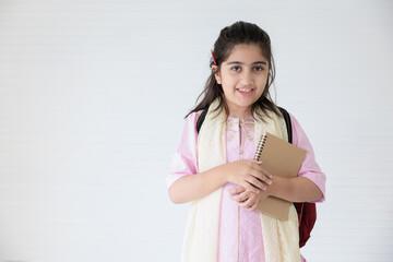 Obraz premium cute indian girl smiling and holding notebook for learning, education concept