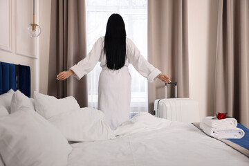 Young woman wearing bathrobe near window in hotel room, back view - obrazy, fototapety, plakaty