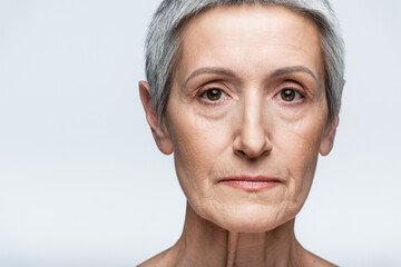 close up of mature woman with grey hair looking at camera isolated on grey