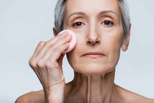 Mature Woman Holding Beauty Sponge And Applying Makeup Foundation Isolated On Grey